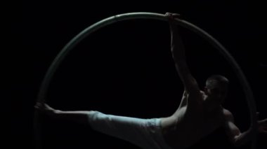 Muscular circus artist perform Cyr Wheel on a black background stage. Concept of motion and movement.