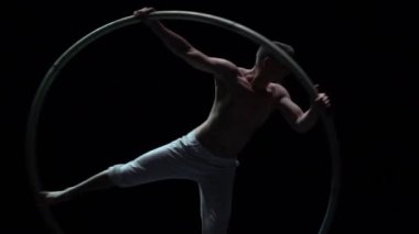 Muscular circus artist perform Cyr Wheel on a black background stage in slow motion.