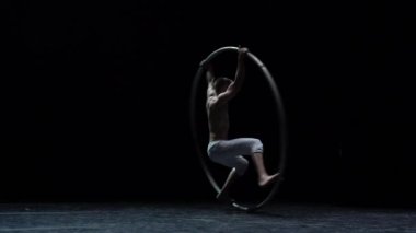 Muscular circus artist perform Cyr Wheel on a black background stage in slow motion.