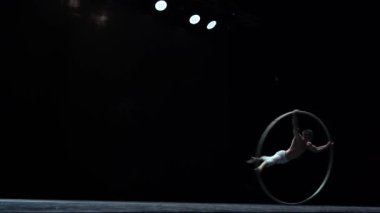 Muscular circus artist perform Cyr Wheel on a black background stage. Concept of motion and movement.
