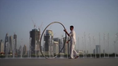 Cyr Wheel artist wearing white Arabic clothing cloth on Dubai cityscape background. Concept of originality, creativity and outstanding.