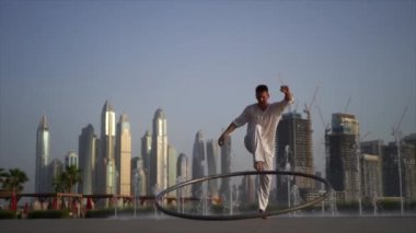 Cyr Wheel artist wearing white Arabic clothing cloth on Dubai cityscape background. Concept of originality, creativity and outstanding.