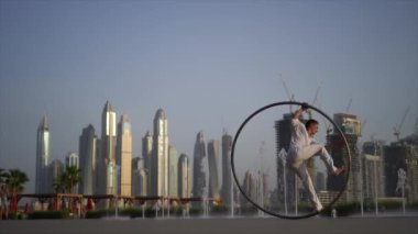 Cyr Wheel artist wearing white Arabic clothing cloth on Dubai cityscape background. Concept of originality, creativity and outstanding.