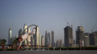 Cyr Wheel artist wearing white Arabic clothing cloth on Dubai cityscape background during sunset. Concept of desire, will and potential 