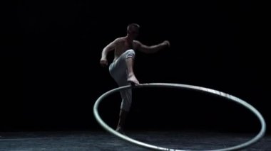 Muscular circus artist perform Cyr Wheel on a black background. Concept of willpower, motivation and healthy lifestyle.