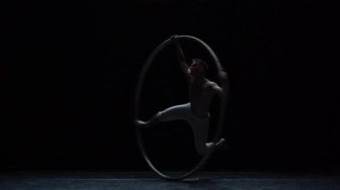 Muscular circus artist perform Cyr Wheel on a black background stage in slow motion.