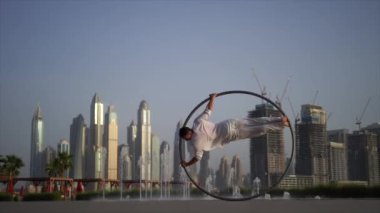 Cyr Wheel artist wearing white Arabic clothing cloth on Dubai cityscape background during sunset. Concept of desire, will and potential 