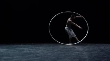 Kaslı sirk sanatçısı siyah arka planda Cyr Wheel performansı sergiliyor. İrade, motivasyon ve tutku kavramı.