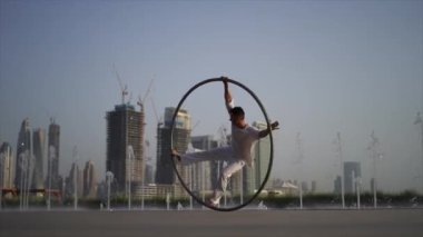 Cyr Wheel artist wearing white Arabic clothing cloth on Dubai cityscape background during sunset