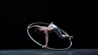 Muscular circus artist perform Cyr Wheel on a black background. Concept of willpower, motivation and healthy lifestyle.