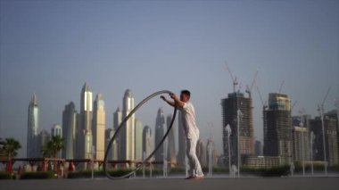 Cyr Wheel artist wearing white Arabic clothing cloth on Dubai cityscape background during sunset