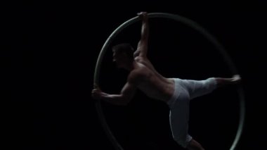 Kaslı sirk sanatçısı siyah arka planda Cyr Wheel performansı sergiliyor. İrade, motivasyon ve tutku kavramı.