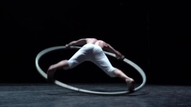 Muscular circus artist perform Cyr Wheel on a black background stage in slow motion.