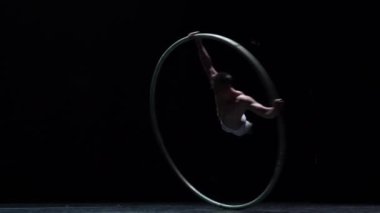 Muscular circus artist perform Cyr Wheel on a black background stage in slow motion.