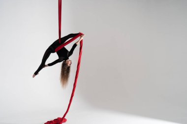 Flexible woman performs on the aerial silk on white background. Concept of originality, creativity and outstanding.