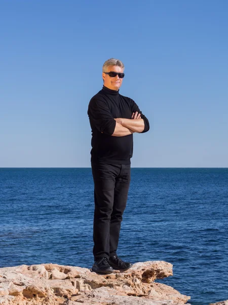 Volwassen zakenman poseren vertrouwen op een rots aan de zee — Stockfoto