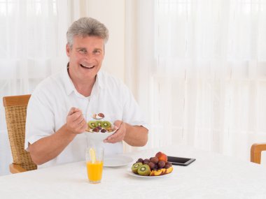 Laughing mature man eating a healthy cereal breakfast clipart