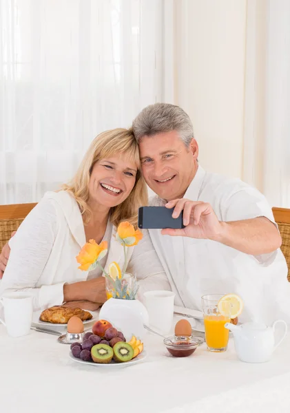 Sağlıklı Kahvaltı yaparken cep telefonlarını selfie fotoğraf çekme mutlu olgun çift — Stok fotoğraf
