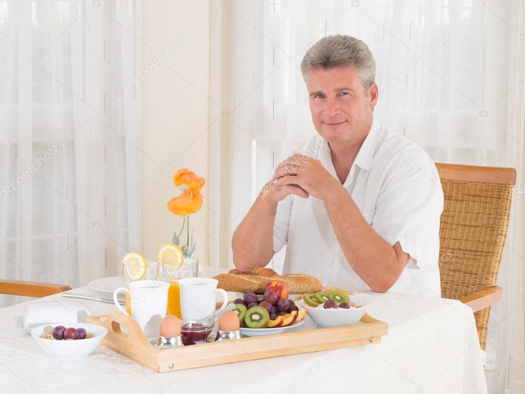 Senior mature man sitting down to a healthy breakfast looking at camera