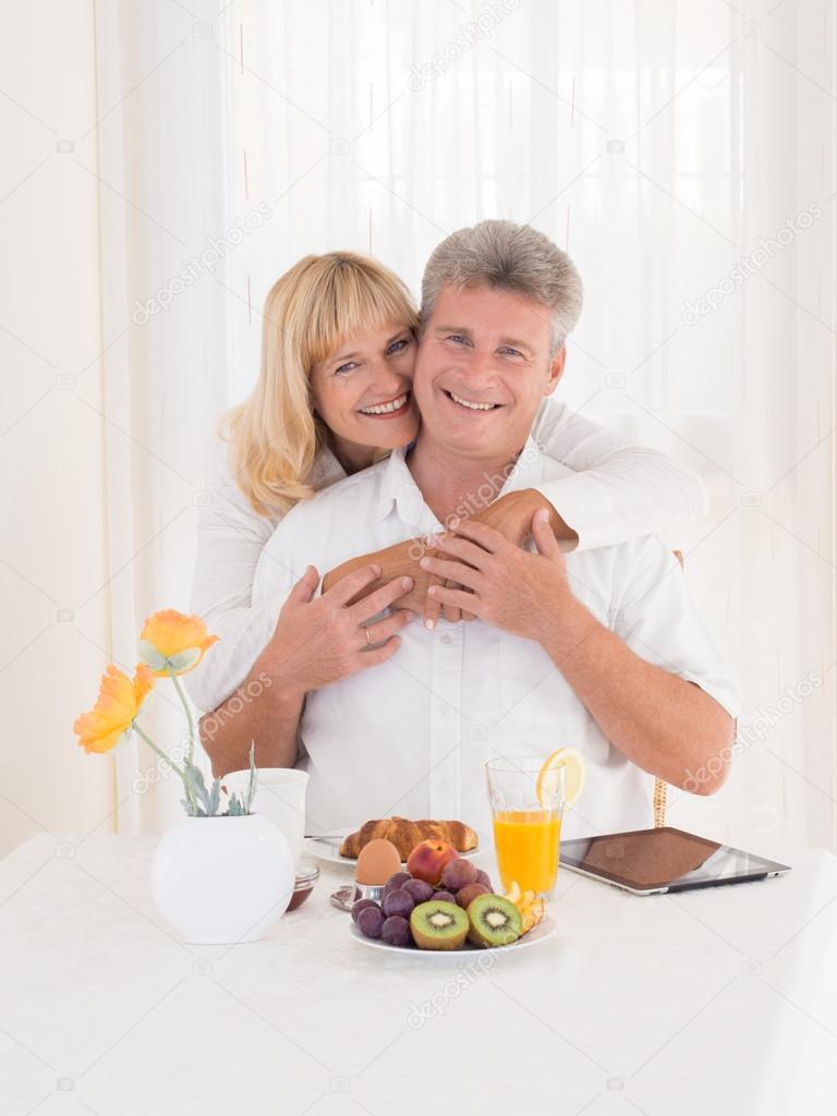 Romantic happy mature couple with beautiful smiles hugging on breakfast