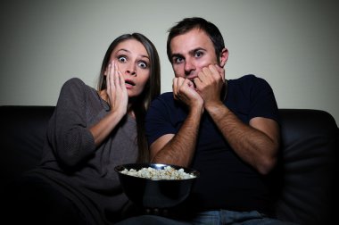 Young couple watching scary movie on tv clipart