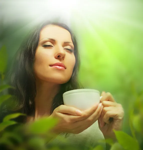 Frau mit Teetasse auf dem Hintergrund verschwommener grüner Blätter — Stockfoto