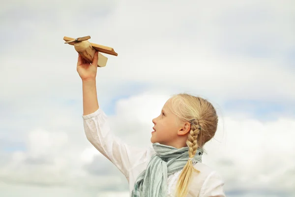 Klein meisje spelen met met een stuk speelgoed vliegtuig tegen de hemel — Stockfoto