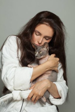 Genç kadın sfenks kedisine sarılıyor.
