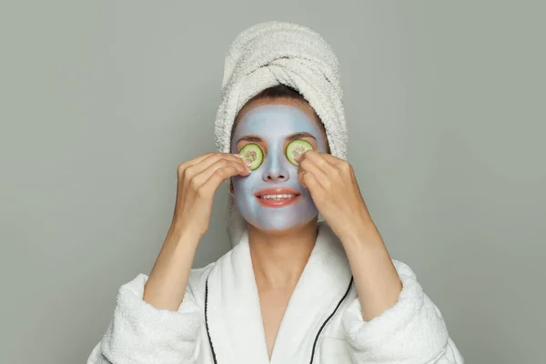 彼女の顔にキュウリのスライスと保湿化粧品フェイスマスクを持つスパの女性 顔の治療とスキンケアの概念 — ストック写真