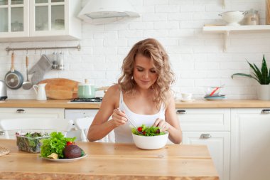 Sağlıklı sarışın kadın içeride sebze salatasıyla kahvaltı hazırlıyor.