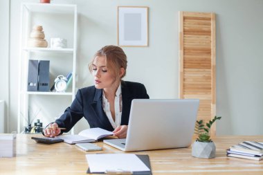 Ofiste not defteri, hesap makinesi ve dizüstü bilgisayar kullanan zeki bir iş kadını.