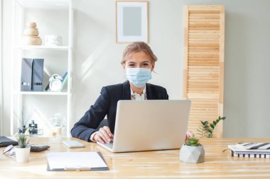 Yönetici kadın masasında çalışıyor ve kovid 19 'a karşı koruyucu bir maske takıyor.