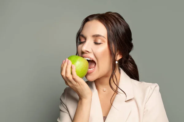 Νεαρή Γυναίκα Δαγκώνει Ένα Πράσινο Μήλο Γκρι Φόντο — Φωτογραφία Αρχείου
