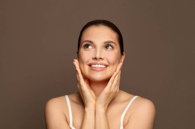 Sağlıklı spa modeli kadın kahverengi arka plana bakıyor.