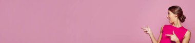 Mutlu sürpriz kadın pembe afiş arkaplanındaki fotokopi alanını işaret ediyor