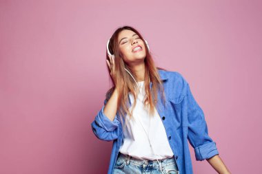 Kulaklıklı neşeli genç bir kadının portresi. Renkli pembe bir arka planda müzik dinliyor.