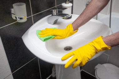 Hands in protective gloves cleaning sink and faucet using microfiber cloth and detergent, concept of housekeeping and hygiene