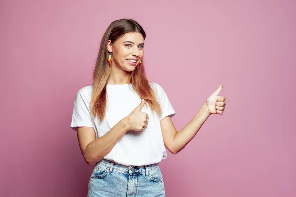 Cheerful hipster woman in white t-shirt making thumb up gesture and smiling joyfully, showing her support and respect to someone. Good job, Well done, I like that concept