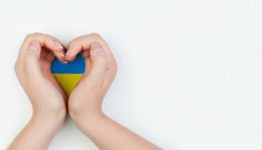 Female hand holding heart with Ukrainian flag on white background. Love Ukraine concept