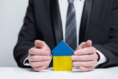Save Ukraine concept. A man protects the house with the flag of Ukraine