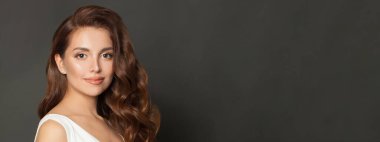 Beautiful young woman with healthy glowy skin and long hair over gray wall background.