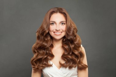Fashion portrait of cute brunette woman with long and shiny wavy hair smiling. Stylish model with brown curly hairstyle