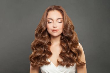 Attractive female model with long and volume shiny wavy hair . Beautiful woman with curly hairstyle and makeup, eyes closed.