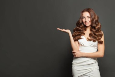 Happy attractive model woman holding empty open palm hand on gray studio wall banner background