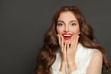 Beautiful happy excited model woman with makeup and long brown curly hair smiling on gray background
