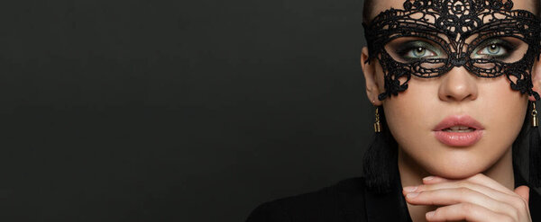 Красивая молодая женщина в черной таинственной венецианской маске на фоне черного баннера. Мода фото