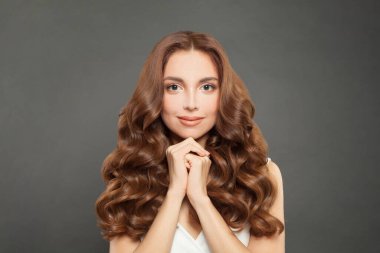 Brunette woman with clean skin and long shiny curly hair. Beautiful fashion model with wavy hairstyle. Care and beauty concept