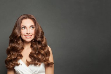 Beautiful brunette lady with long shiny wavy brown hair looking up on black background with copy space