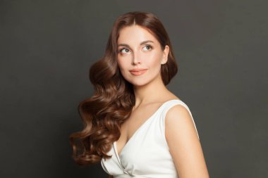 Attractive fashion model with long shiny wavy brown hair looking up. Portrait of beautiful woman brunette on black background