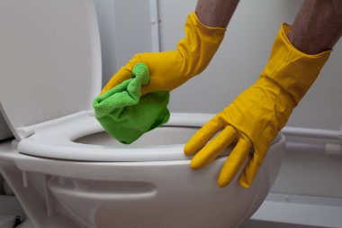 Close up photo of hands wearing yellow gloves cleaning a white WC toilet